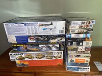 Stack of various boxed scale model kits including P-51B Mustang, M3 Grant tank, and Yorktown missile cruiser, plus multiple military miniature figure kits.