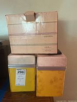 Three cases stacked together: two yellow metal cases with pink lids and a cardboard box on top labeled for floppy disks, all holding 45 RPM records.