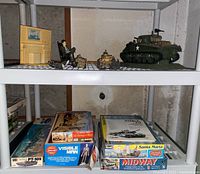 Shelf setup with assembled tank and ship models, figurines, and board game/model kit boxes underneath.