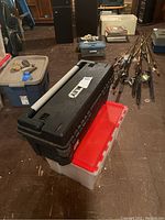 Stacked storage containers including a black Stanley Pro Toolbox and a white/red tote with rocks and minerals, fishing rods and other boxes in background.