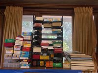 Photo shows stacked boxes and a black rack holding numerous model train car boxes, featuring brands Bowser, Athearn, Red Caboose, MEC, and Accurail. Several brightly colored freight model train cars visible on rack.