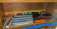 Shelf with model train cars arranged in rows, including silver passenger cars and various colored freight and tank cars.
