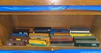 Collection of HO scale model train freight cars displayed in a wooden shelf, showing various paint schemes and logos.
