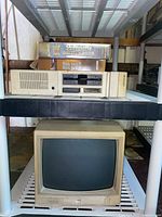 Vintage beige IBM desktop computer tower on shelf with dual floppy drives. Beige IBM CRT monitor below.