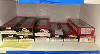 Shelves with boxed HO scale freight train cars in red and black Atlas packaging including Evans Double Plug Door Box Cars and PS-2 Covered Hoppers