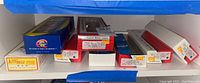 Shelf storage of multiple boxed model train cars from various brands showing front face and box designs with price stickers.