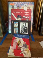 Paper doll books and framed wall art displayed together showing the variety of items included in the lot.