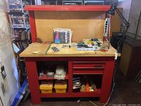 Front view of red metal workbench with pegboard, drawers, and tool contents visible on tabletop and shelves.