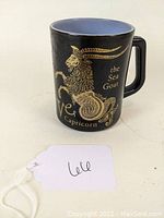 Front and side view of the black coffee mug showing the gold Capricorn zodiac sign, the Sea Goat image and text.