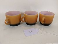 Front and side view of the 3 Fire King coffee cups arranged in a row showing handles and fade color.
