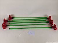 Top-down view of six glass flower stems laid in parallel, showing their green stems and red flower heads.