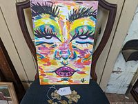 Full view of the abstract portrait painting on canvas placed on a chair showing the vibrant colors and artist signature.