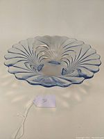 Blue translucent glass bowl with scalloped edge and swirling fan-like pattern, four feet visible from an angled side view.