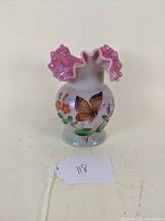 Front view showing the butterfly and flower decorations on the cranberry glass vase with ruffled pink rim.