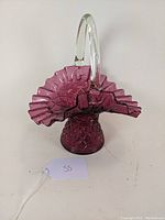Front angled view of cranberry glass basket showing ruffled rim, diamond optic pattern base, and clear handle.