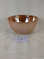 Front and side view of the peach luster Fire King glass mixing bowl showing swirl pattern and small scuff on side.