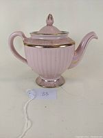 Front angle view of pink Hall China teapot with gold accents on ribbed body and lid, showing handle and spout.