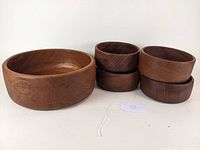 Photo showing one large teak oval salad bowl and four smaller round teak bowls stacked together on a white surface.