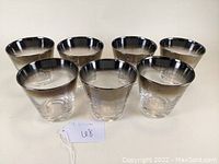 Seven mid century old fashioned tumblers with silver fading on rim, arranged in two rows showing shape and detail.