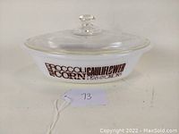 Oval white opaque glass casserole dish with clear glass lid featuring brown vegetable names in stylized fonts printed on side