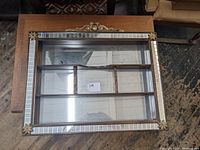 Top-down view of the rectangular wooden shadow box display case showing the multiple inner compartments, mirrored back, and decorative corner rosettes on the outer edge.