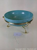Turquoise round glass bowl on gilt metal stand showing front and side profiles.