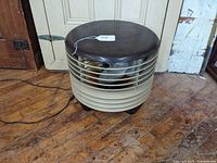 Full front view of round mid-century fan with beige grille and brown cushioned top.