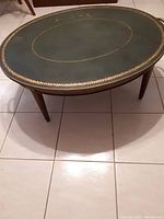 Wide view of wooden oval coffee table showing dark green leather top with gold decorative pattern and wooden legs
