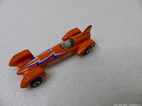 Side angled view of the orange Kenner Turbo Tram 82 toy car showing lightning bolt decals and driver in cockpit.