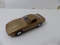 Metallic gold 1986 Chevrolet Corvette dealer promotional model car displayed on white background showing side and top angle details.