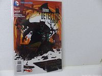 Front cover of Detective Comics #34 showing Batman in a dark silhouette against an orange background with bats and gravestones, issue details and writers Manapul and Buccellato.