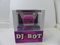 Front view of the boxed DJ-Bot showing the pink speaker with eye-like design inside clear packaging marked DJ-BOT by LiteHawk.