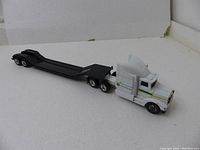 White John Deere branded semi truck cab with black flat trailer, showing side and front angles to highlight condition and details.