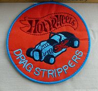 Top view of a circular embroidered Hot Wheels patch with 'Drag Strippers' and a dragster car design, orange background with blue border.