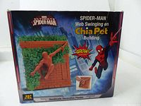 Front of box showing image of the Spider-Man Chia Pet planter with greenery growing on it. Branding and product name visible, emphasizing the web swinging Spider-Man and chia plant building.