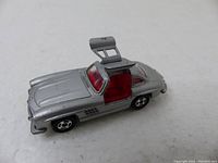 Side view of the silver Tomica Mercedes Benz 300SL model car showing open gullwing door and red interior.