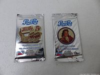 Two sealed silver foil vintage Pepsi collectible trading card packs, one with a stack of Pepsi bottles and 5 cent label, the other with a woman's portrait.