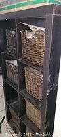 Black wooden 8-cubby storage unit with 7 natural wicker baskets inside, one basket missing and some damage visible on basket handles and unit surfaces.