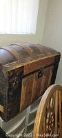 Front view of large antique wooden steamer trunk with curved top, showing wood slats, metal hardware, and aged leather handle remnants.