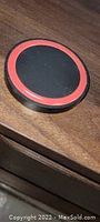 Photo of circular wireless charger with black surface and red rim on a wooden surface.