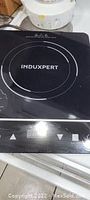 Top view of the induction burner showing the Induxpert logo and heating zone markings on the glass surface.