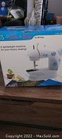 Photo of boxed lightweight sewing machine with brand and marketing text visible on box.