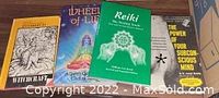 Four spiritual books arranged on a wooden surface, titles visible: Witchcraft, Wheels of Life, Reiki, The Power of Your Subconscious Mind