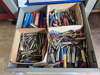 Drawer with multiple cardboard boxes containing assorted metal tool bits, many with blue and red plastic tubes and metal holders.