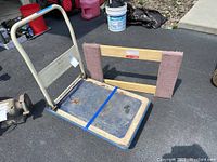 Wide view of wood movers dolly and metal cart together outdoors on black asphalt.