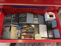 Open red drawer showing four gray metal index cases, jar of loose bits, metal block, Ondura box