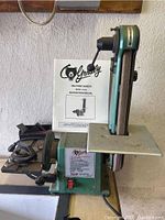 Front and side view of Grizzly Belt/Disc Sander with instruction manual placed behind the belt sander.