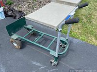 Side perspective of green metal hand truck cart showing base plate, large rear wheels and caster wheel front.