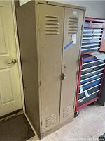 Closed view of the beige two-door metal locker cabinet with ventilation slots and locking latch.