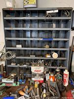 Front view of metal organizer cabinet with shelves holding various small parts and containers, showing wear and some rust.